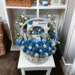 A colorful and organized baby gift basket tailored for new moms, with a focus on a soft onesie and a set of baby booties.
