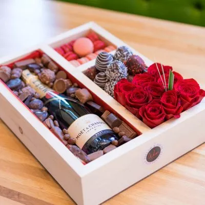 Luxury gift box featuring premium champagne, fresh bouquet of flowers, gourmet macaroons, and decadent chocolate-covered strawberries.