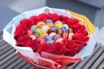 Gourmet bouquet emphasizing the textures of roses and macarons.