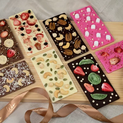 Assortment of 8 gourmet chocolate bars in dark, milk, white, and pink colors, elegantly displayed with visible inclusions of freeze-dried berries, nuts, marshmallows, and dried fruits, reflecting the luxury and variety of the collection