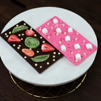 Image of artisanal chocolate bars: dark chocolate with dried kiwi & strawberries, and pink white chocolate with marshmallows.