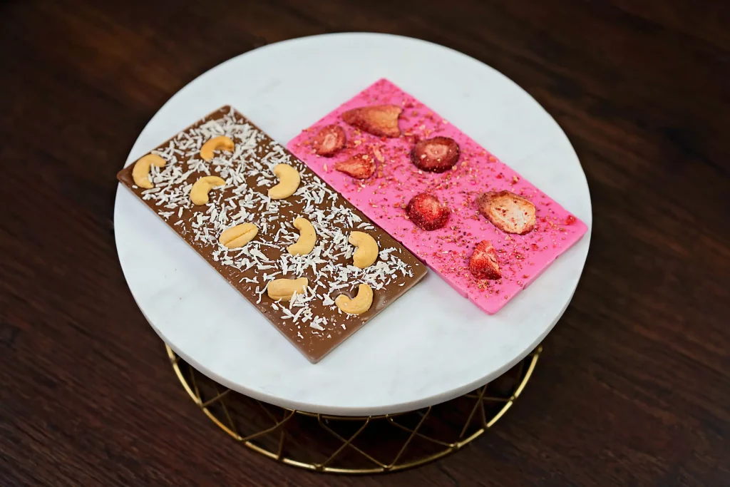 Image of exquisite duo chocolate bars: milk chocolate with nuts & coconut, and pink-colored white chocolate with strawberries.