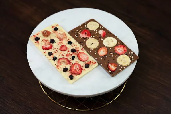 Image of two artisanal chocolate bars: creamy white chocolate with freeze-dried strawberries, raspberries, and blueberries, and rich milk chocolate with freeze-dried strawberries and bananas.
