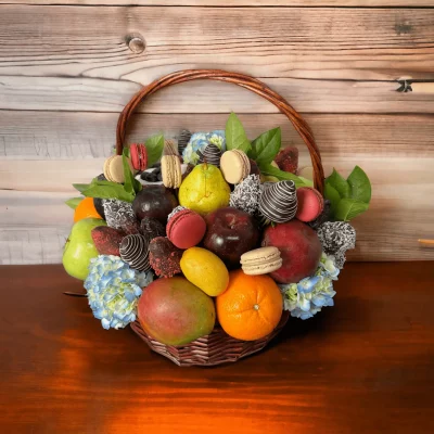 Overhead shot of a bountiful fruit basket filled with fresh, assorted fruits and floral elegance, highlighted by chocolate covered strawberries and macarons.