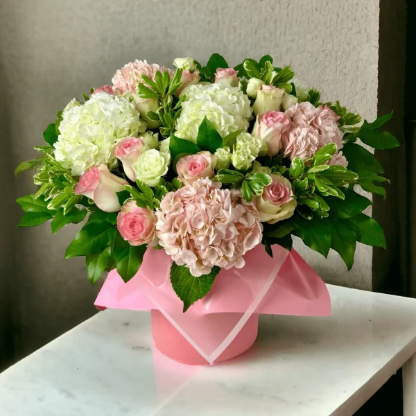 An exquisite floral arrangement called Flower Box Allure, encased in a hat box and blending pink roses with hydrangeas for a stunning visual effect.