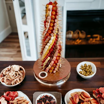 A towering Charcuterie Tower centerpiece, featuring layers of cheeses and meats, with dried tomatoes and olives, set against an NYC skyline backdrop.